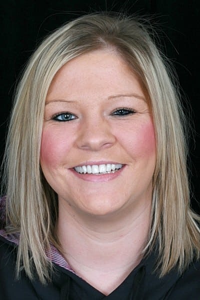 Smiling woman with blonde hair against black background.