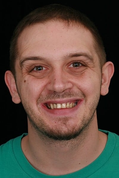 Smiling man in a teal shirt against black background.