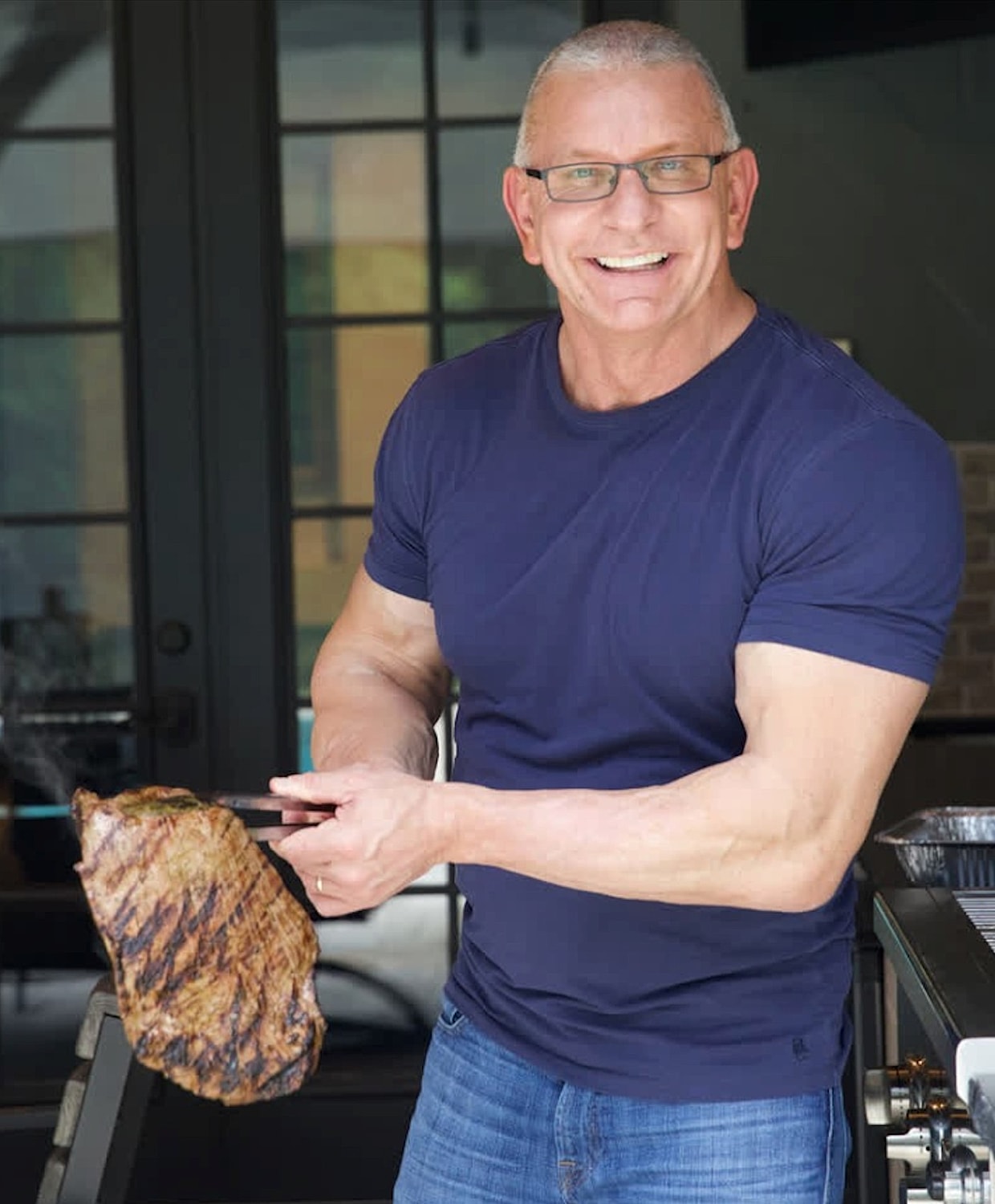 Man grilling steak outdoors, smiling confidently.
