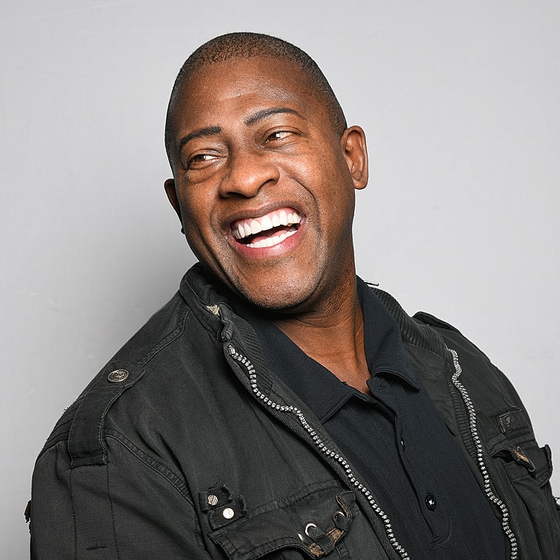 Smiling man in black jacket against gray background.