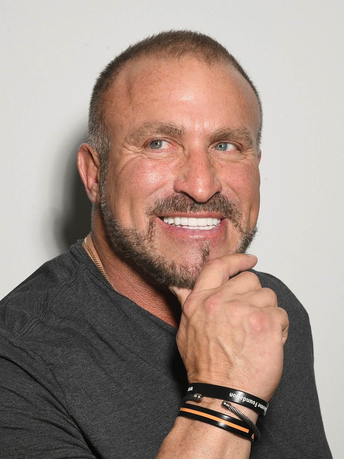 Smiling man with beard and bracelets posing.