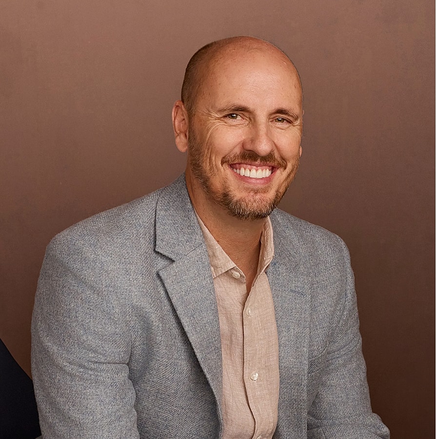 Smiling man in a grey blazer portrait.