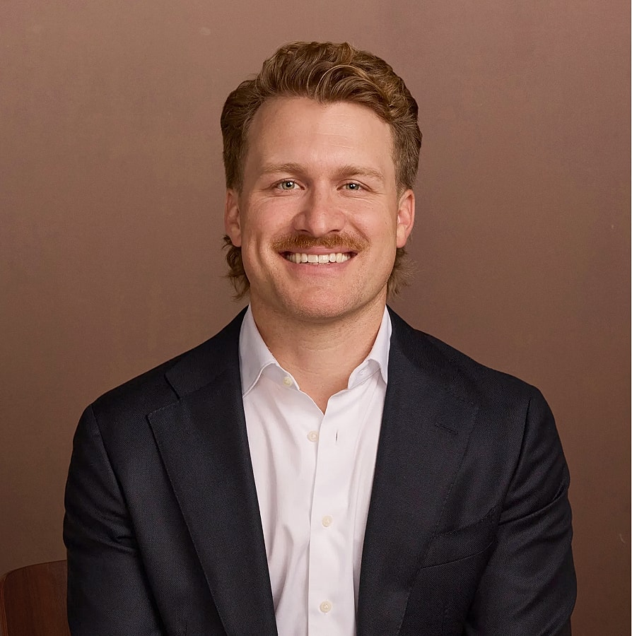 Smiling man in suit against a brown background.