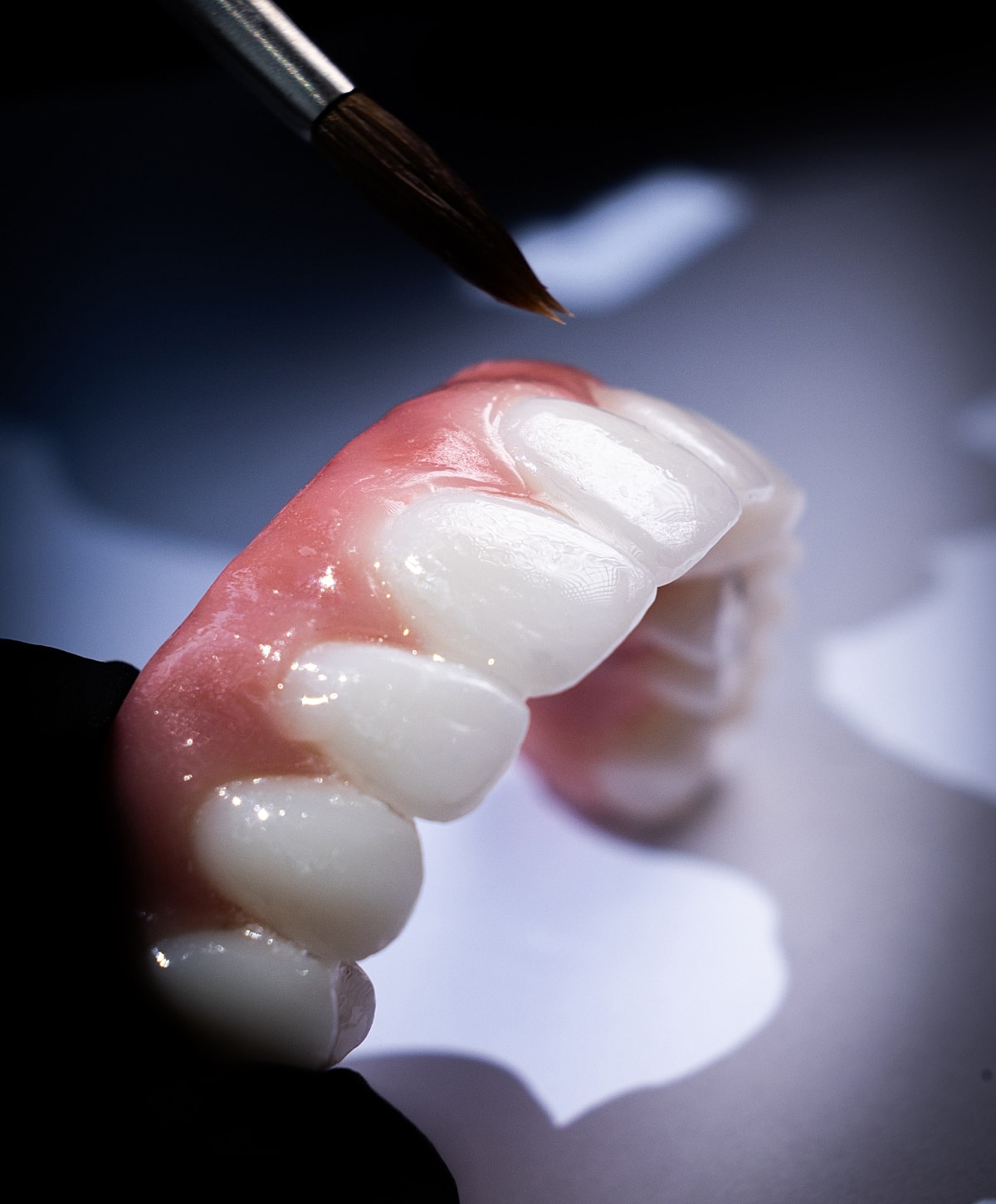Dental prosthetic being painted with a brush.