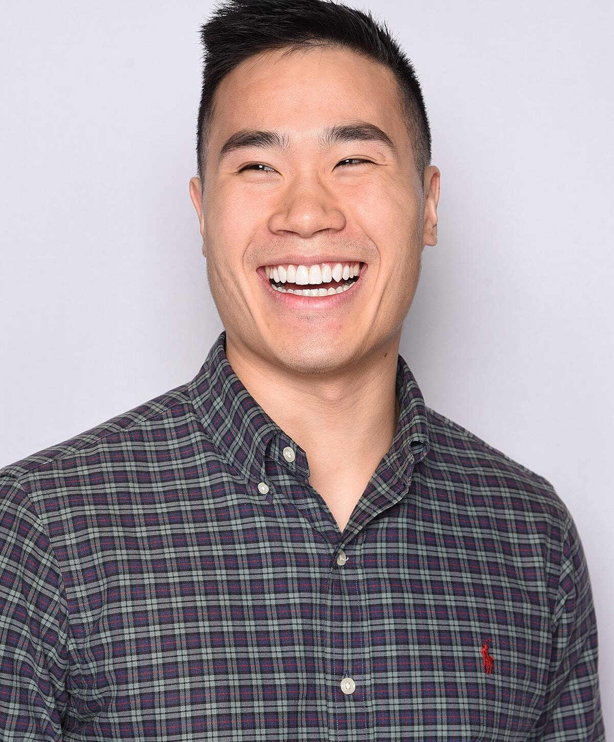 Smiling man in plaid shirt against light background.