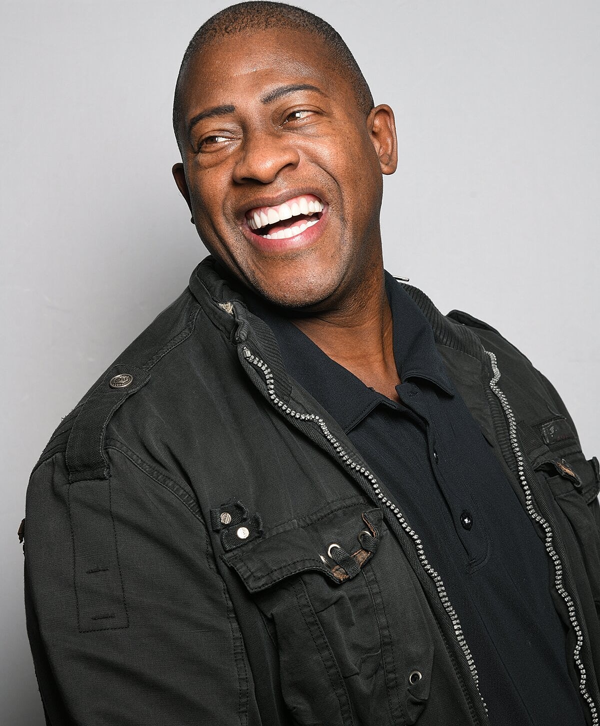 Smiling man in a black jacket against gray background.
