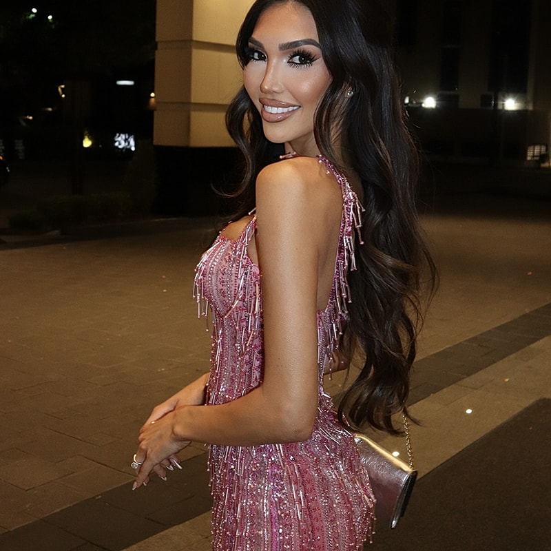 Woman in glamorous pink dress smiling outdoors.