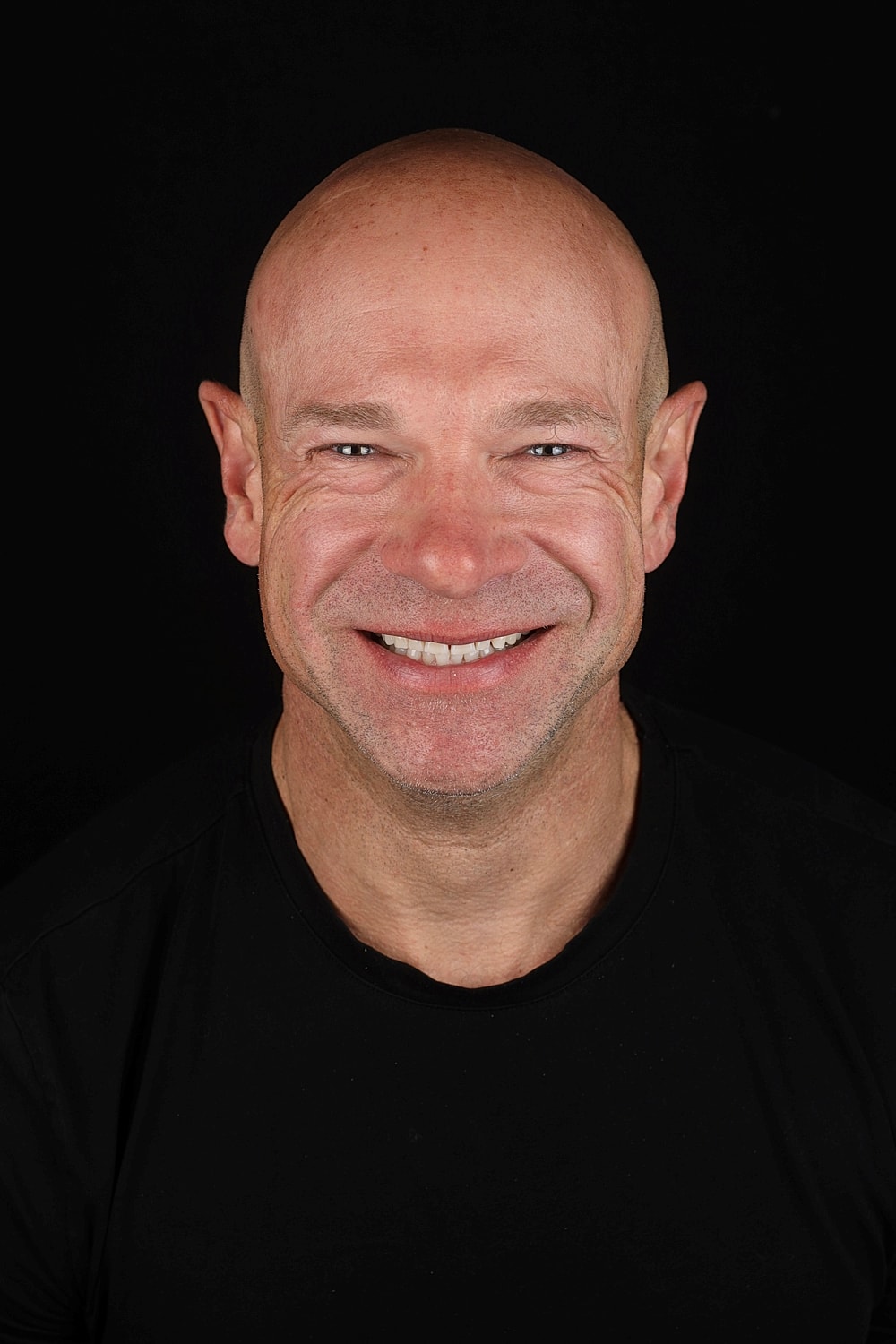 Smiling bald man against black background.