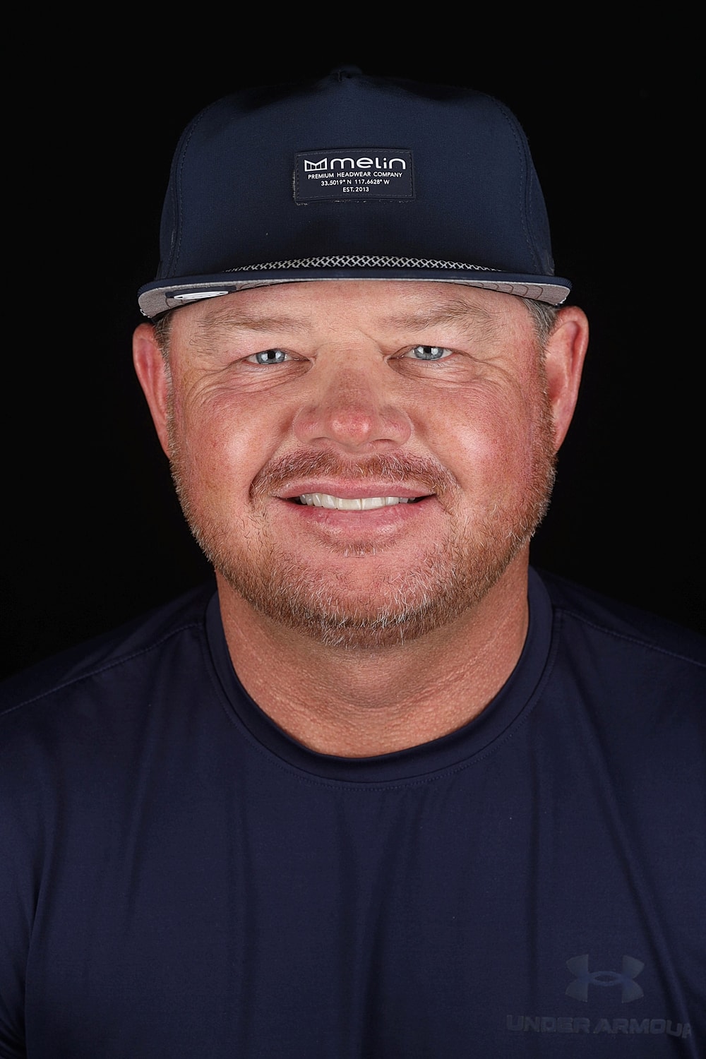 Smiling man wearing a dark baseball cap.