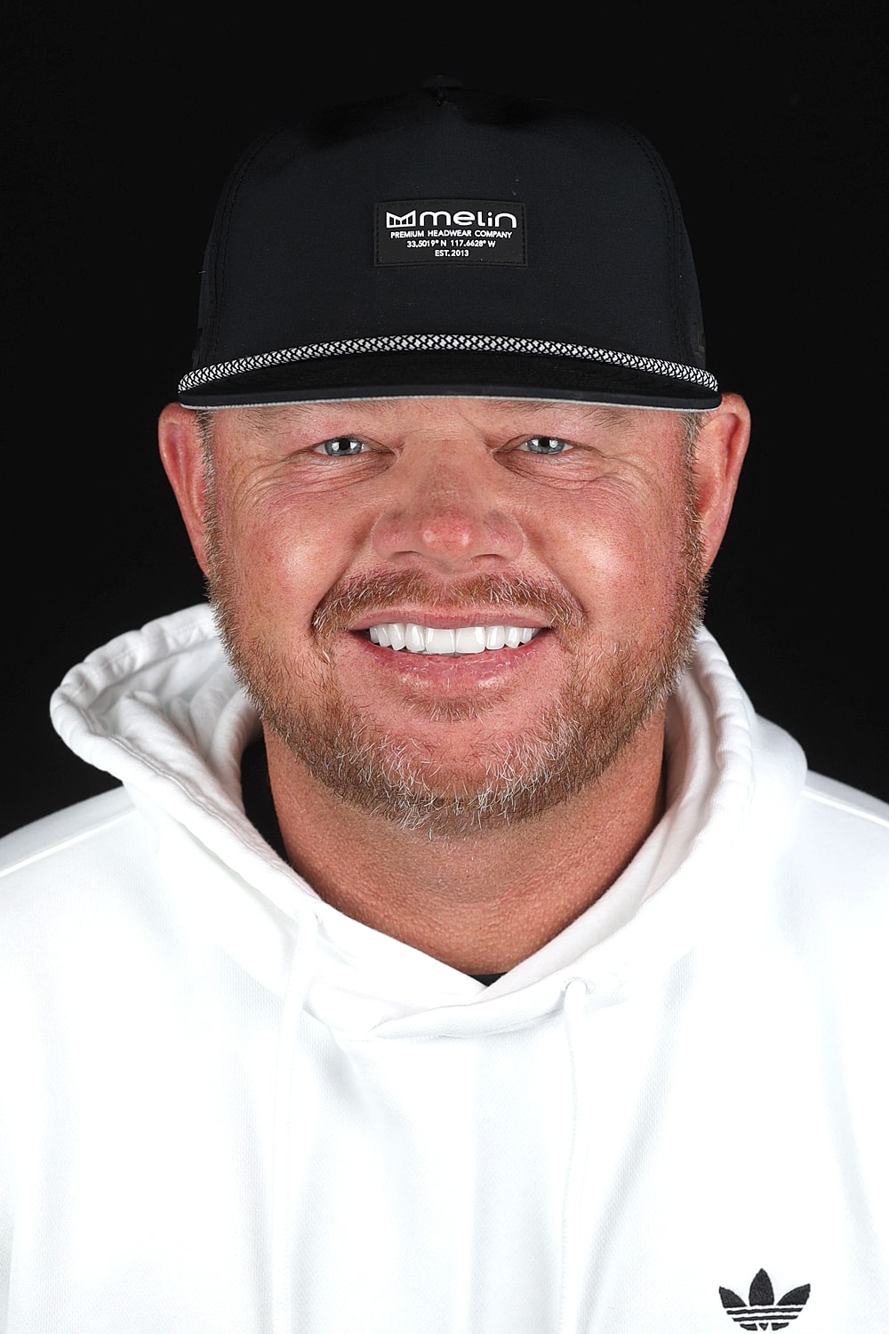 Smiling man in a black cap and white hoodie.