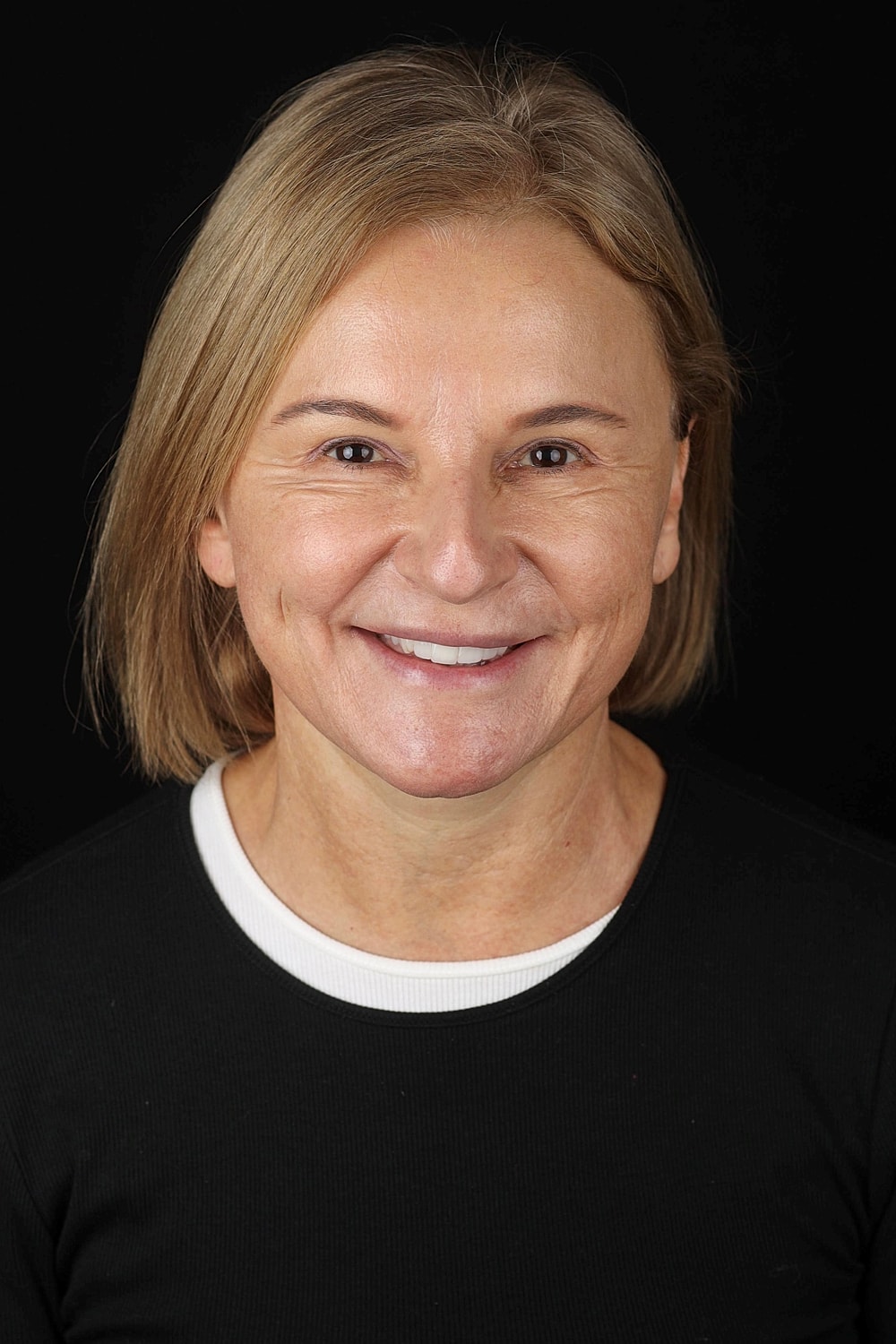 Smiling woman with short blonde hair, black background.