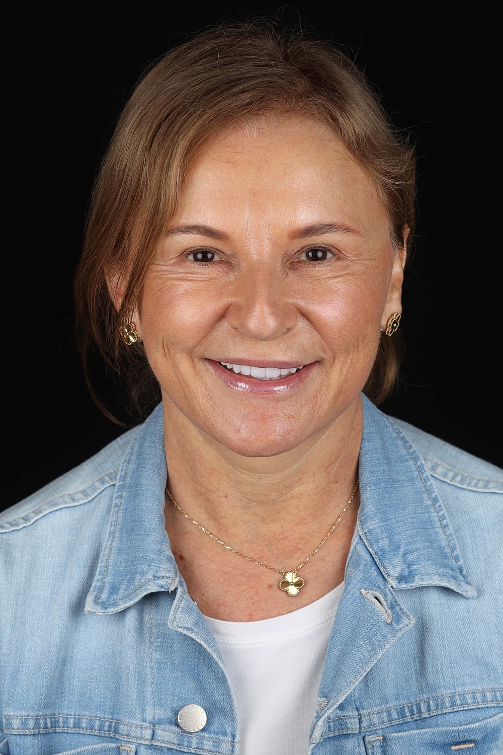 Smiling woman in denim jacket against black background.