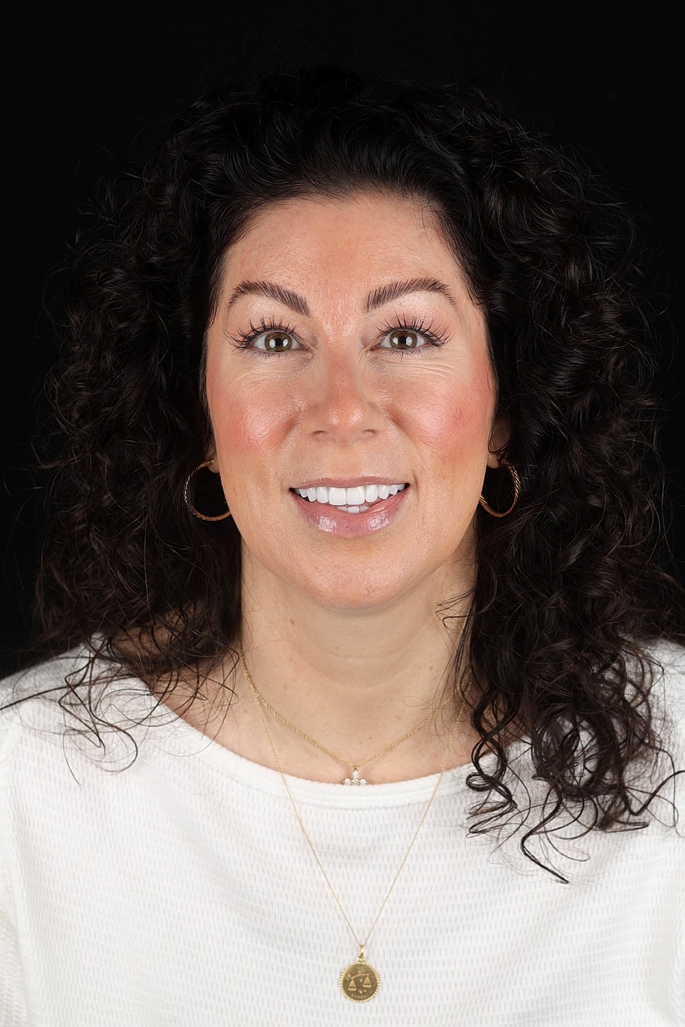 Smiling woman with curly hair against black background.