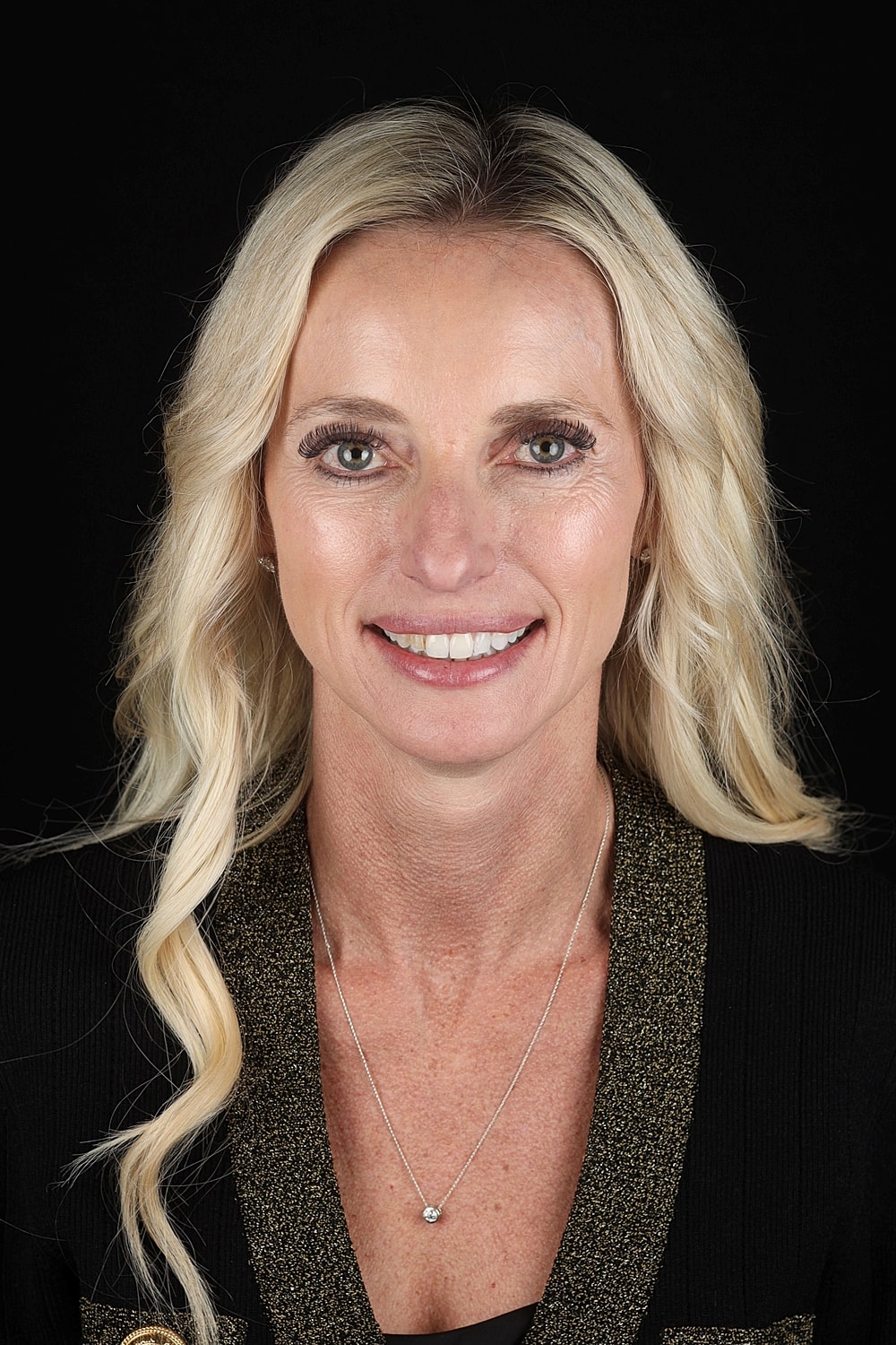 Smiling woman with long blonde hair against black background.