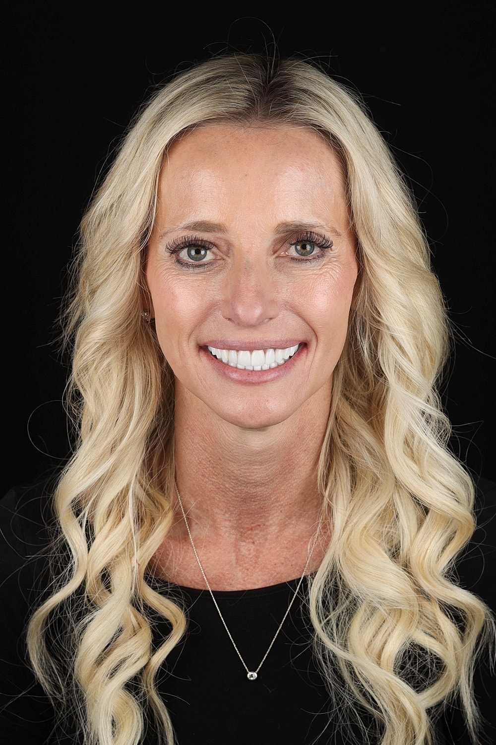 Smiling woman with long blonde hair, black background.