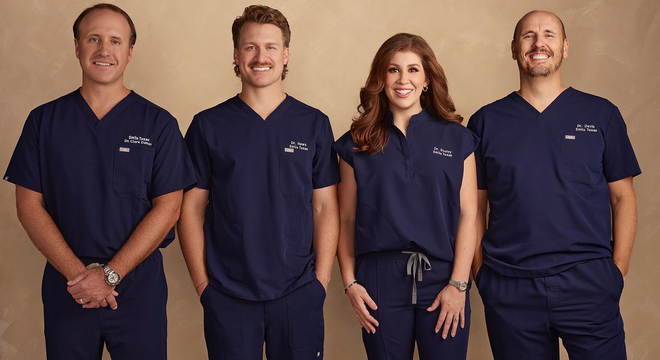 Dental team in navy scrubs smiling together.