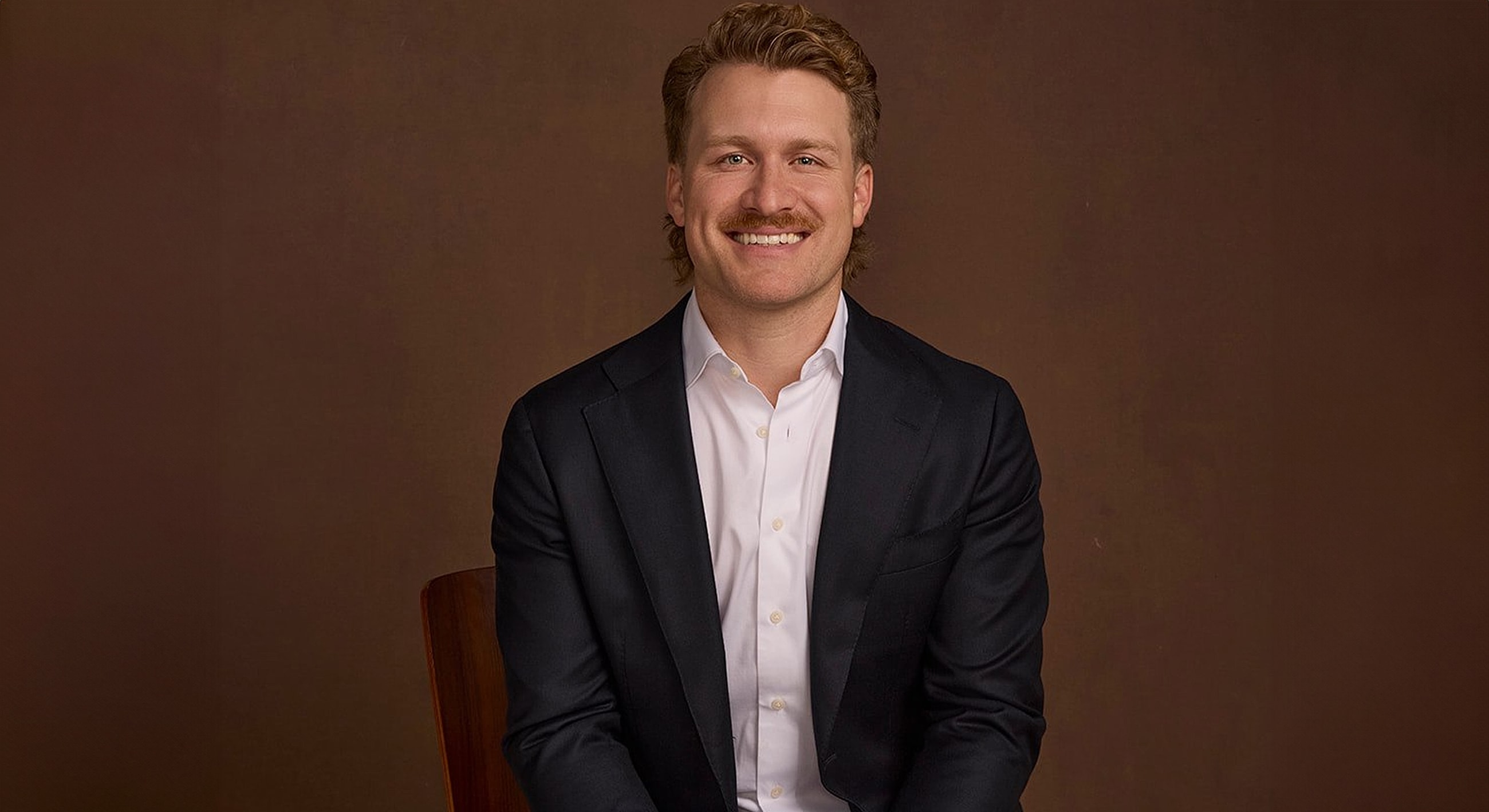 Smiling man in suit against a brown background.