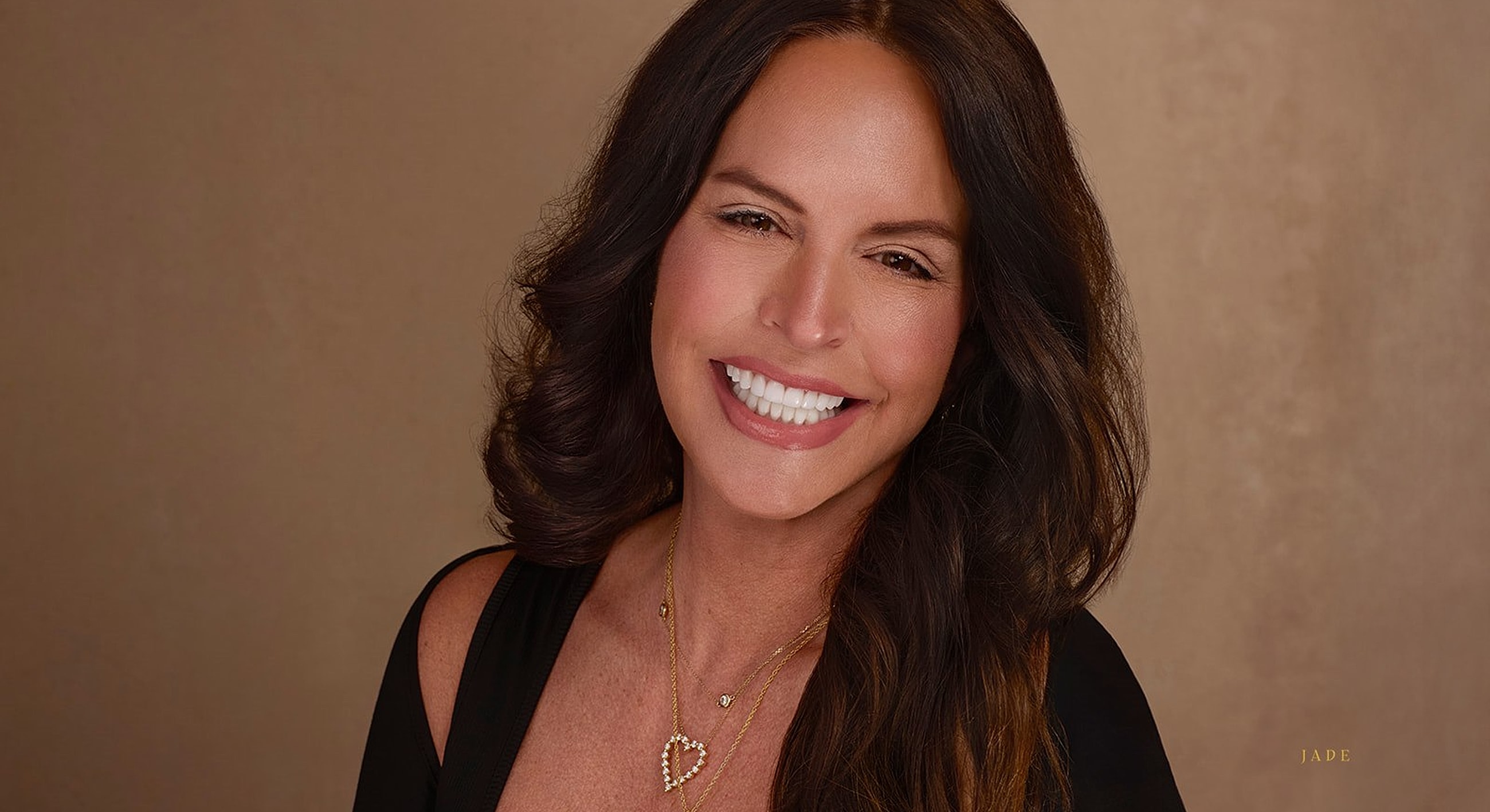 Smiling woman with long brown hair and necklaces.