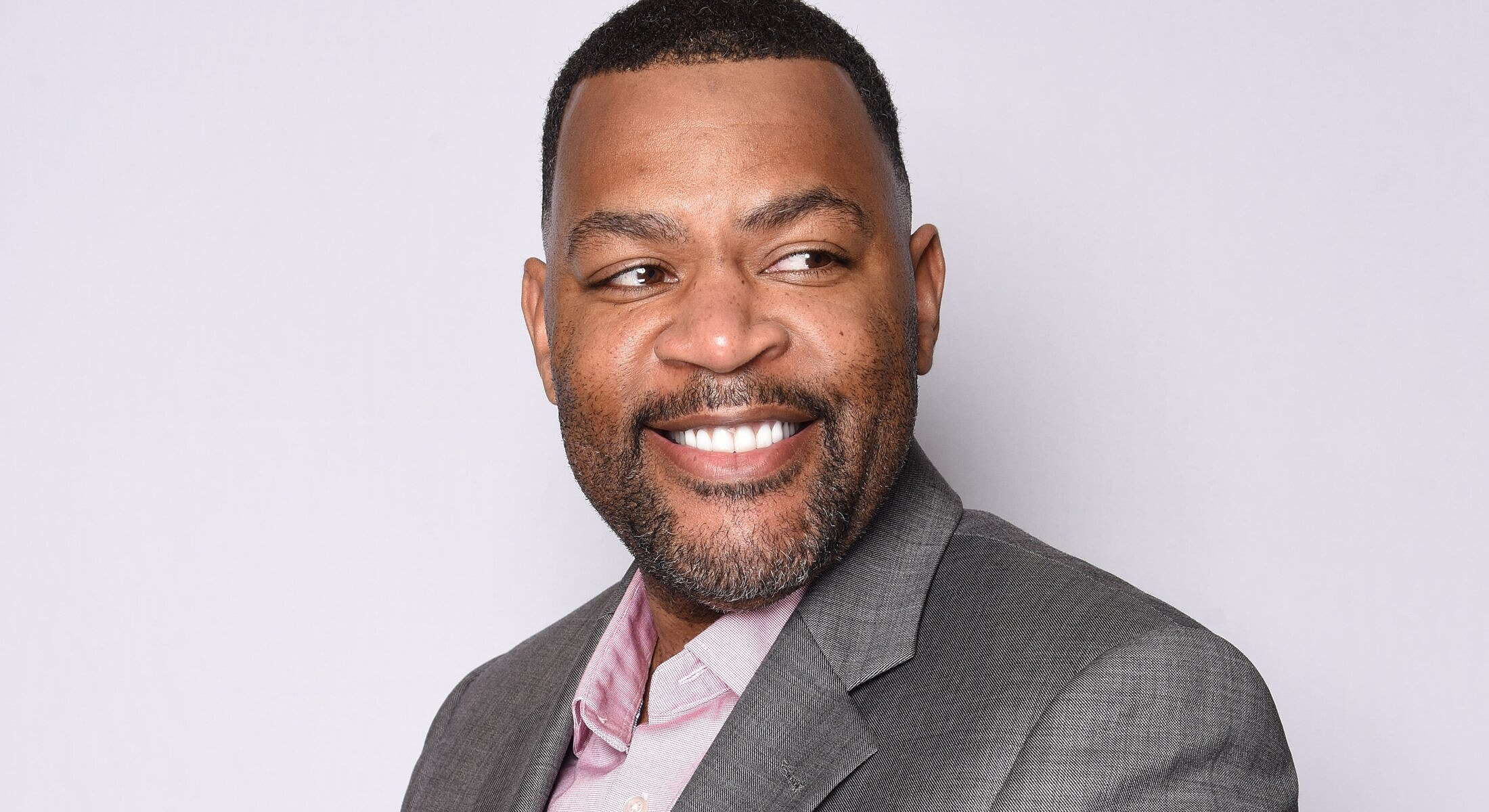 Smiling man in a suit against a plain background.