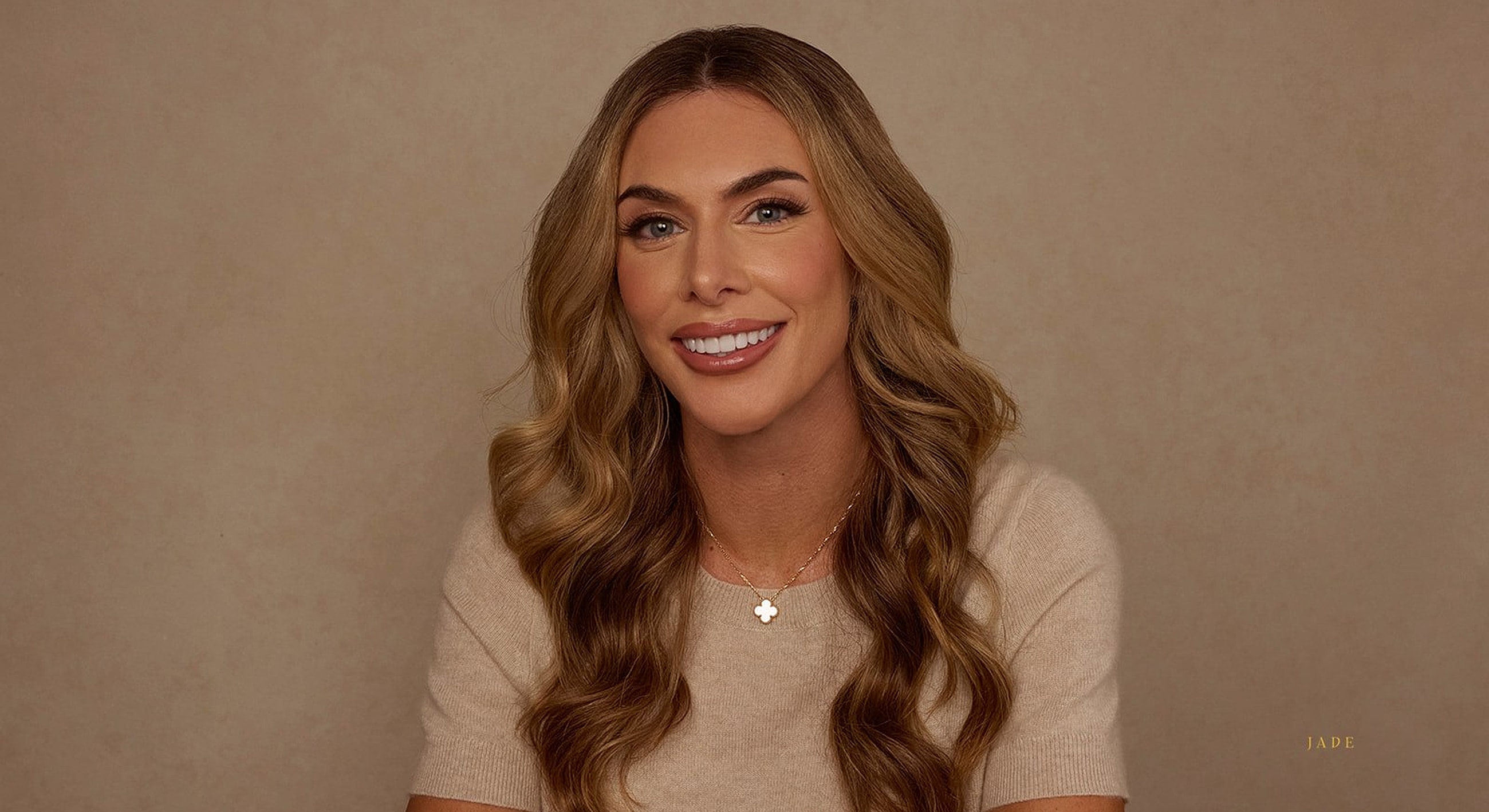 Smiling woman with wavy hair on neutral background.