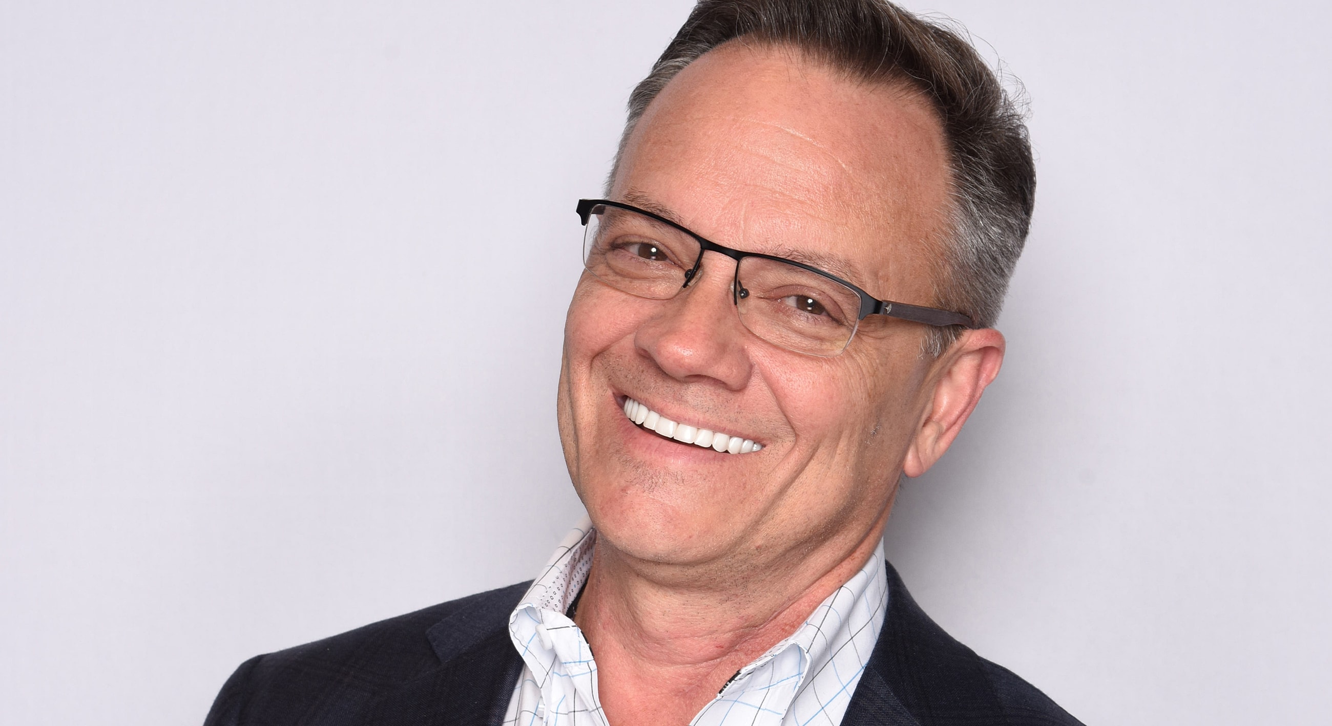 Smiling man with glasses against plain background.